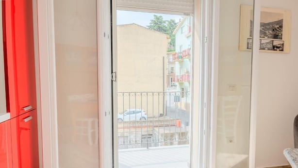 Ein Zimmer mit einer Schiebeglastür, die auf einen Balkon führt, einem roten Schrank und einem gerahmten Bild an der Wand.