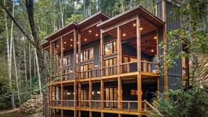 A multi-level cabin with a wooden exterior, multiple balconies, and large windows. - Luxury Creekfront | 3 King Suites | Hot Tub (East Ellijay)
