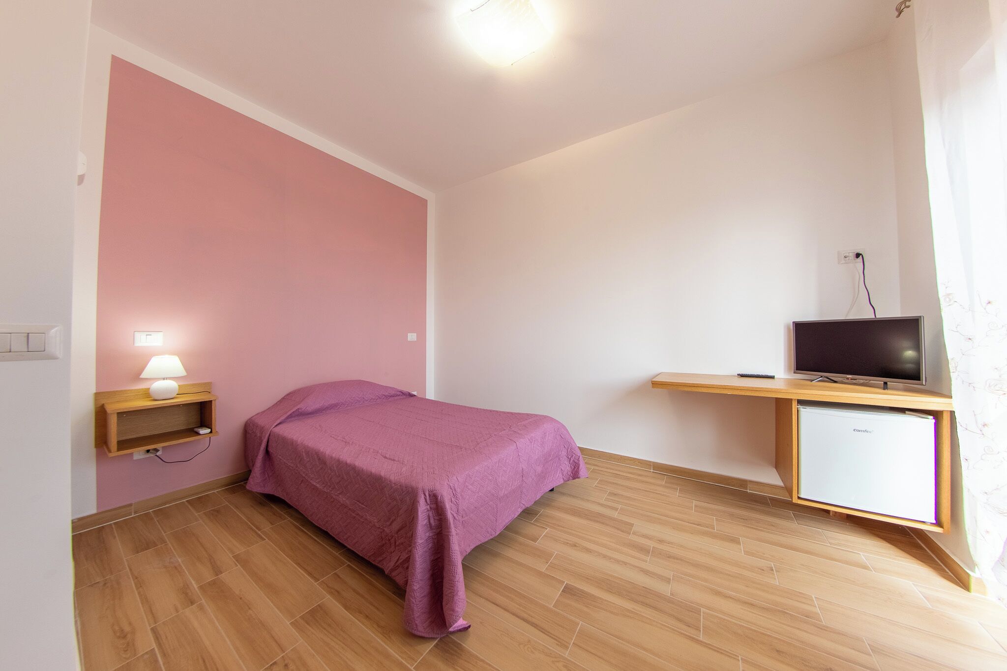 Un dormitorio con una cama, televisión, escritorio y lámpara.