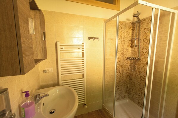 Un baño con un lavamanos blanco, cabina de ducha con mampara de vidrio y un perchero para toallas.