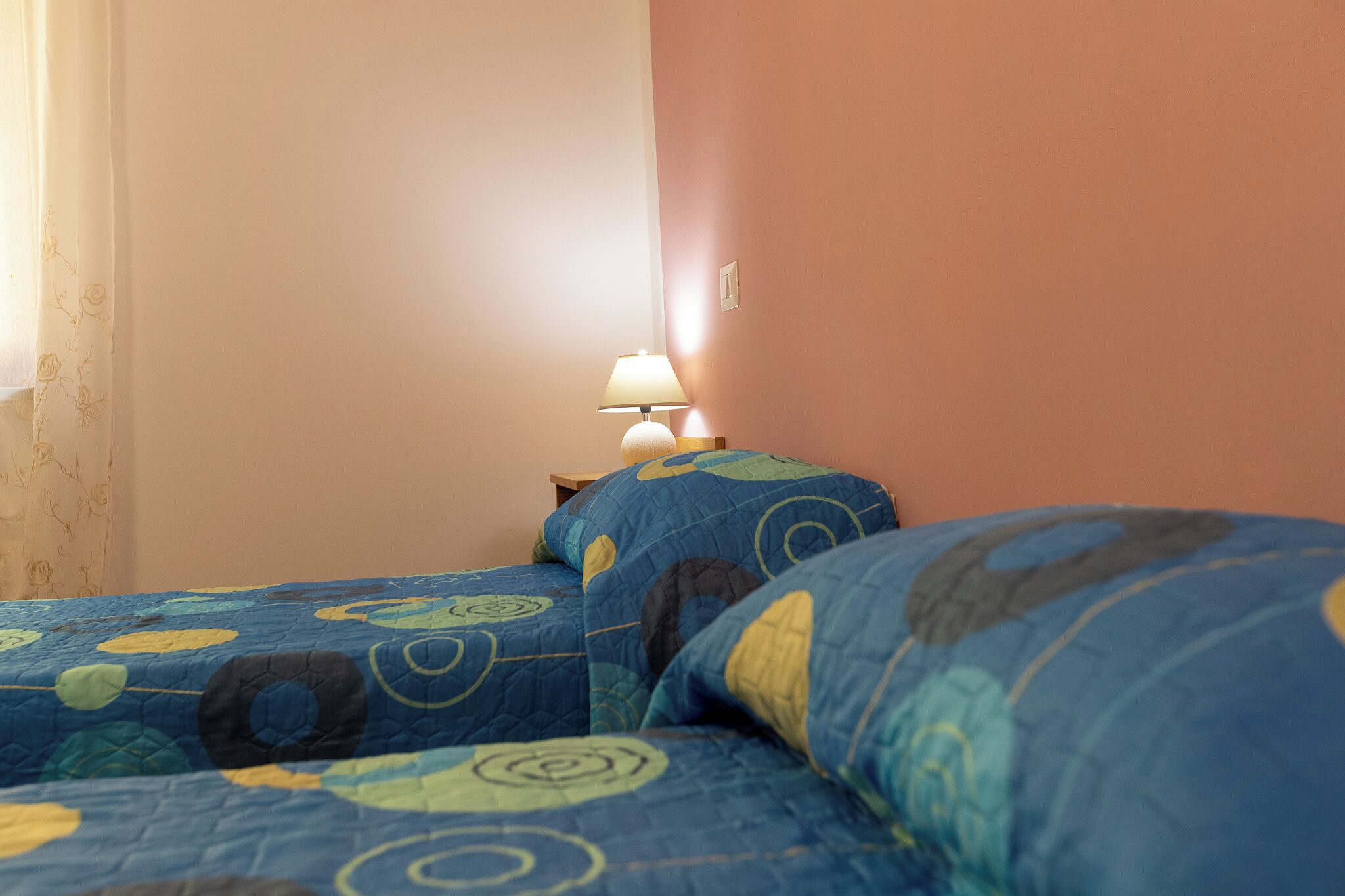 A bedroom with two beds, a nightstand, and a lamp.