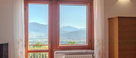 Habitación con un amplio ventanal que ofrece vistas a la montaña, un radiador debajo de la ventana y un armario de madera a la derecha.