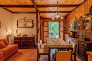 A cozy wooden interior with a dining table, chairs, a sofa, and a kitchen area with cabinets and a hanging light fixture. - Appartamento Fonte Eremita (Roccaraso)