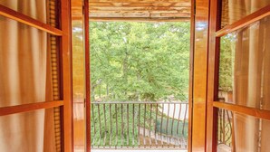Ein hölzerner Balkon mit Metallgeländer, der Blick auf einen grünen, belaubten Baum freigibt.