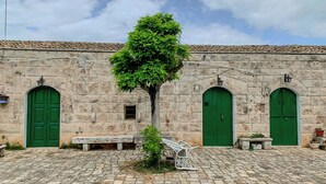 Une cour avec un bâtiment en pierre doté de trois portes vertes et d’un banc.