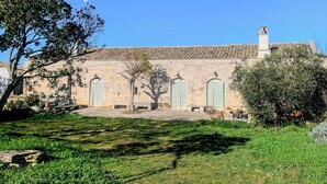 Un bâtiment doté d’un toit recouvert de tuiles, d’une cheminée et d’un jardin avec de la pelouse et des arbres.