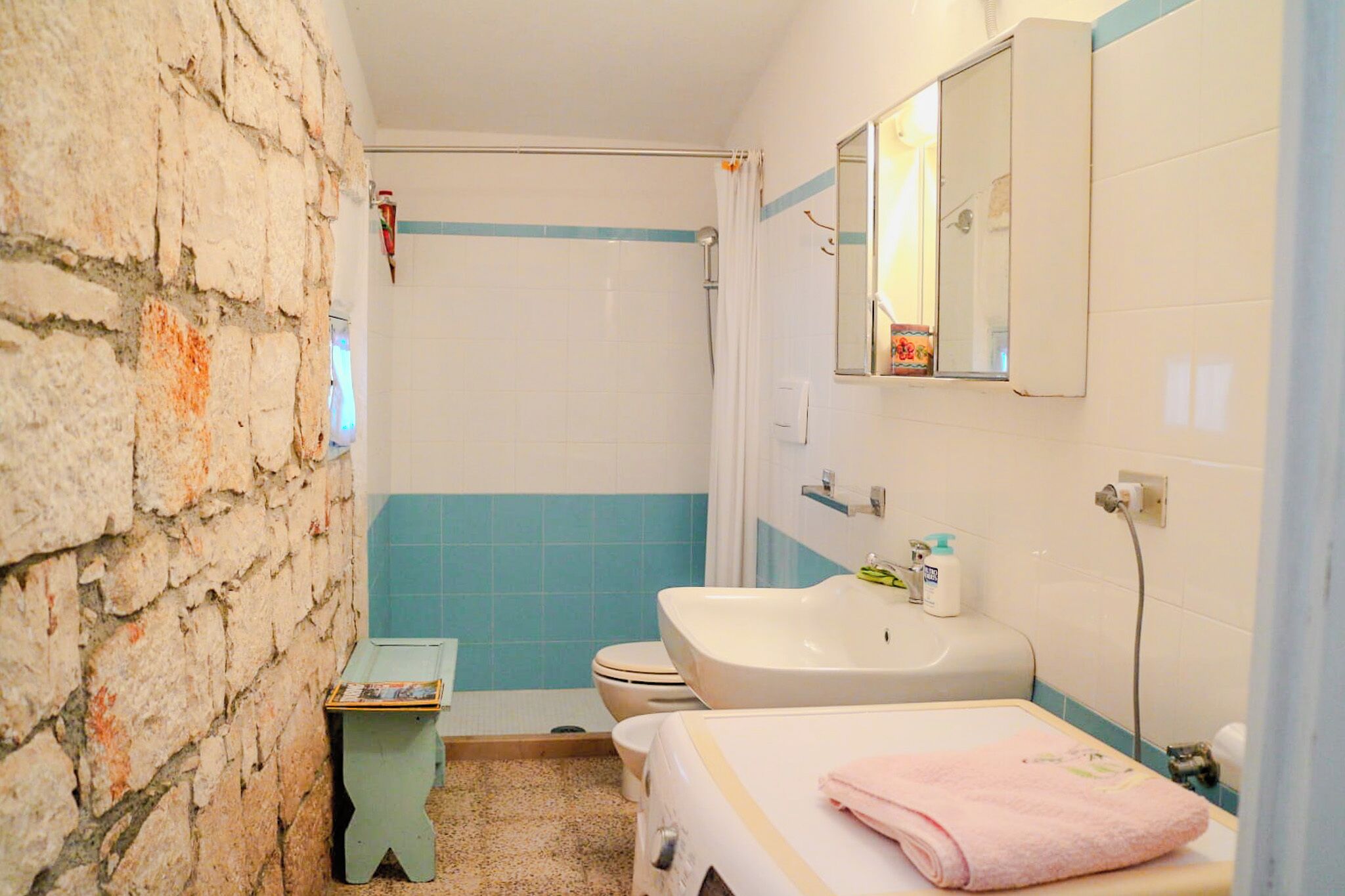 Een badkamer met een stenen muur, een witte wasbak, een spiegel en een toilet.