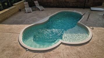 A swimming pool with a unique shape, a stone wall, and a few lounge chairs.