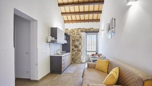 A compact living space with a kitchenette, a stone archway, a sofa with cushions, and a dining area. - Casale Sammartano By L.A.Apartments (Ummari)