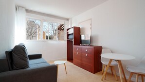 Ein modernes Wohnzimmer mit einem grauen Sofa, einem kleinen runden Tisch und einem Fernseher auf einer Holzkassette.