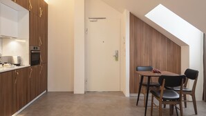 A modern kitchen with wooden cabinets and a built-in oven. There is a dining area with a table and chairs. - LSA Avenida by Numa (Lisbon)