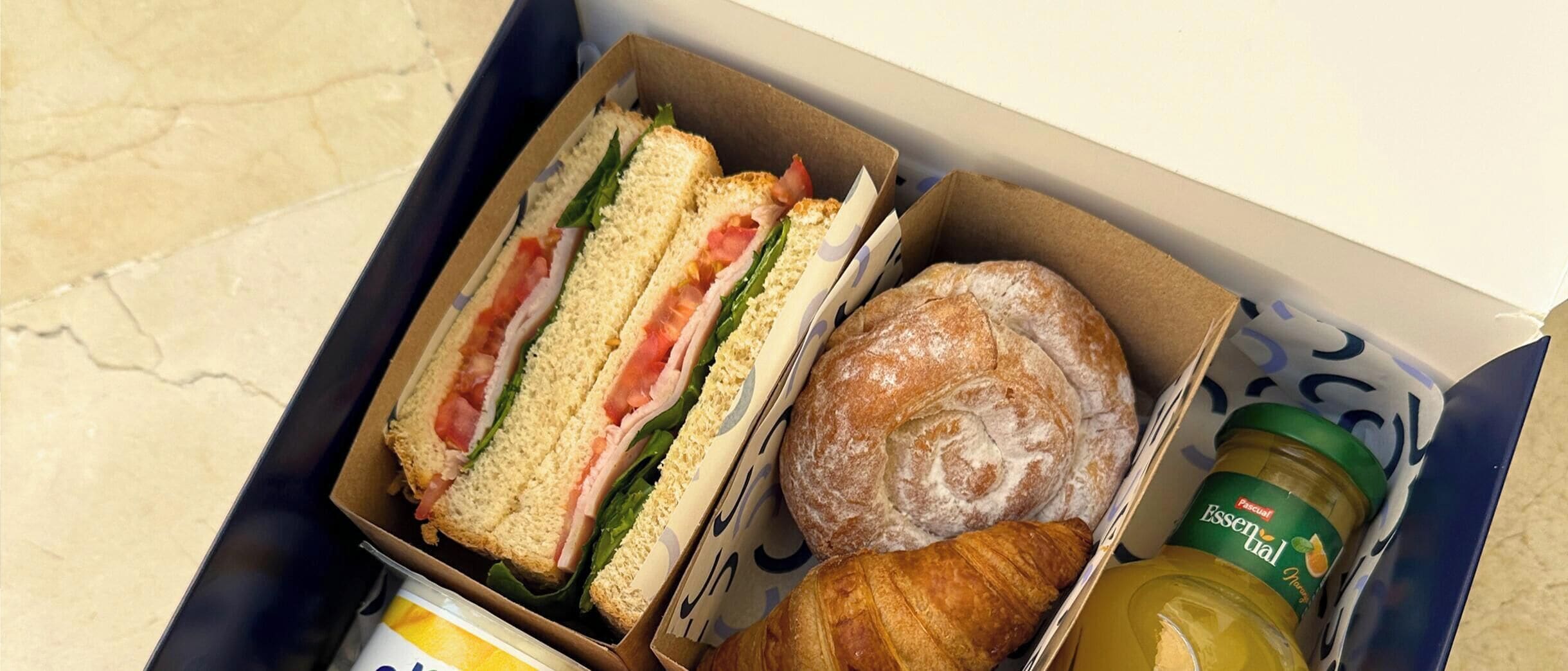 Een doos met een sandwich, een croissant en een pot mosterd.