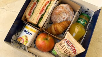 Une boîte à lunch contenant des sandwichs, un croissant, une pomme, une bouteille de jus de fruits, un pot de yaourt et un sachet de pain.