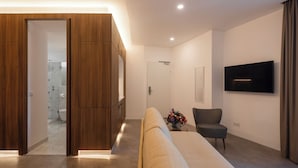 A modern hotel room with a large bed, a seating area, a TV mounted on the wall, and a wooden wardrobe. - LSA Avenida by Numa (Lisbon)