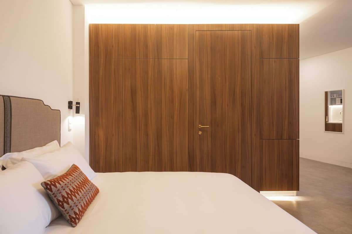 Een moderne slaapkamer met een groot bed, een houten garderobe en een nachtkastje met een lamp.