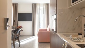 A modern kitchen with a built-in microwave, a sink, and a countertop. There is a dining area with a table and chairs, and a pink sofa in the background. - LSA Avenida by Numa (Lisbon)