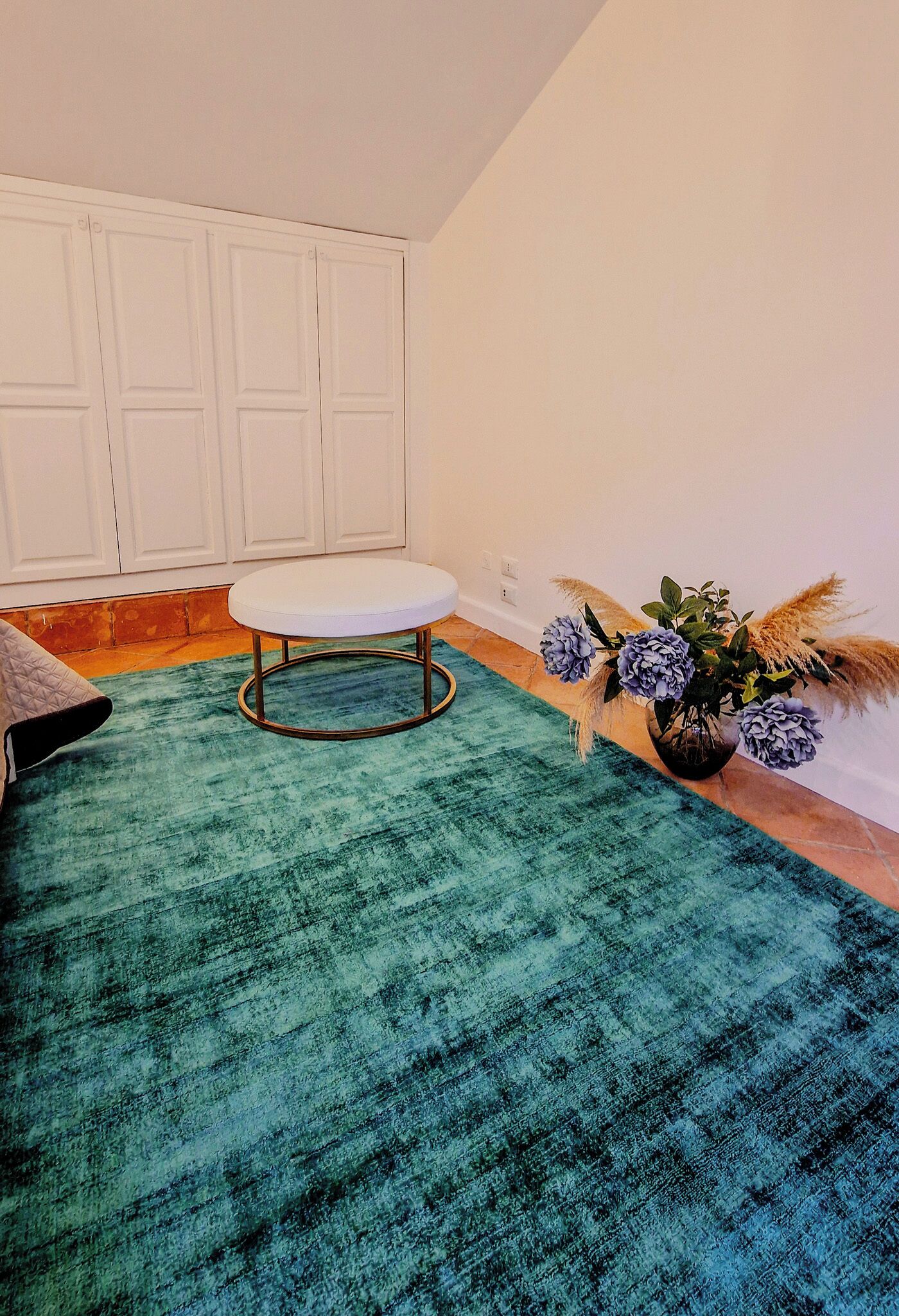 Une pièce avec un tapis de couleur turquoise, un banc blanc, un vase rempli de fleurs et un meuble blanc.