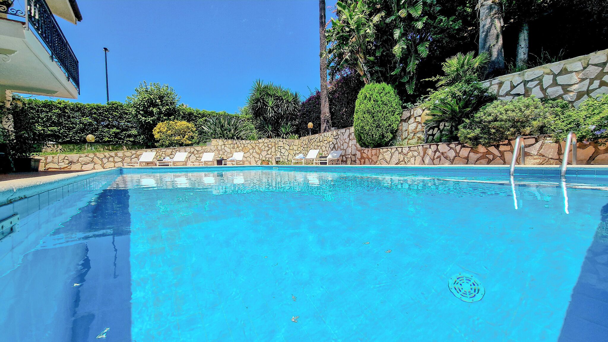 Una piscina azul cristalina con sillones de descanso y un muro de piedra.