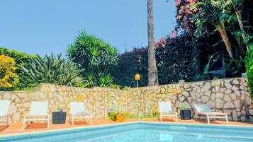 A clear swimming pool with lounge chairs and a stone wall.