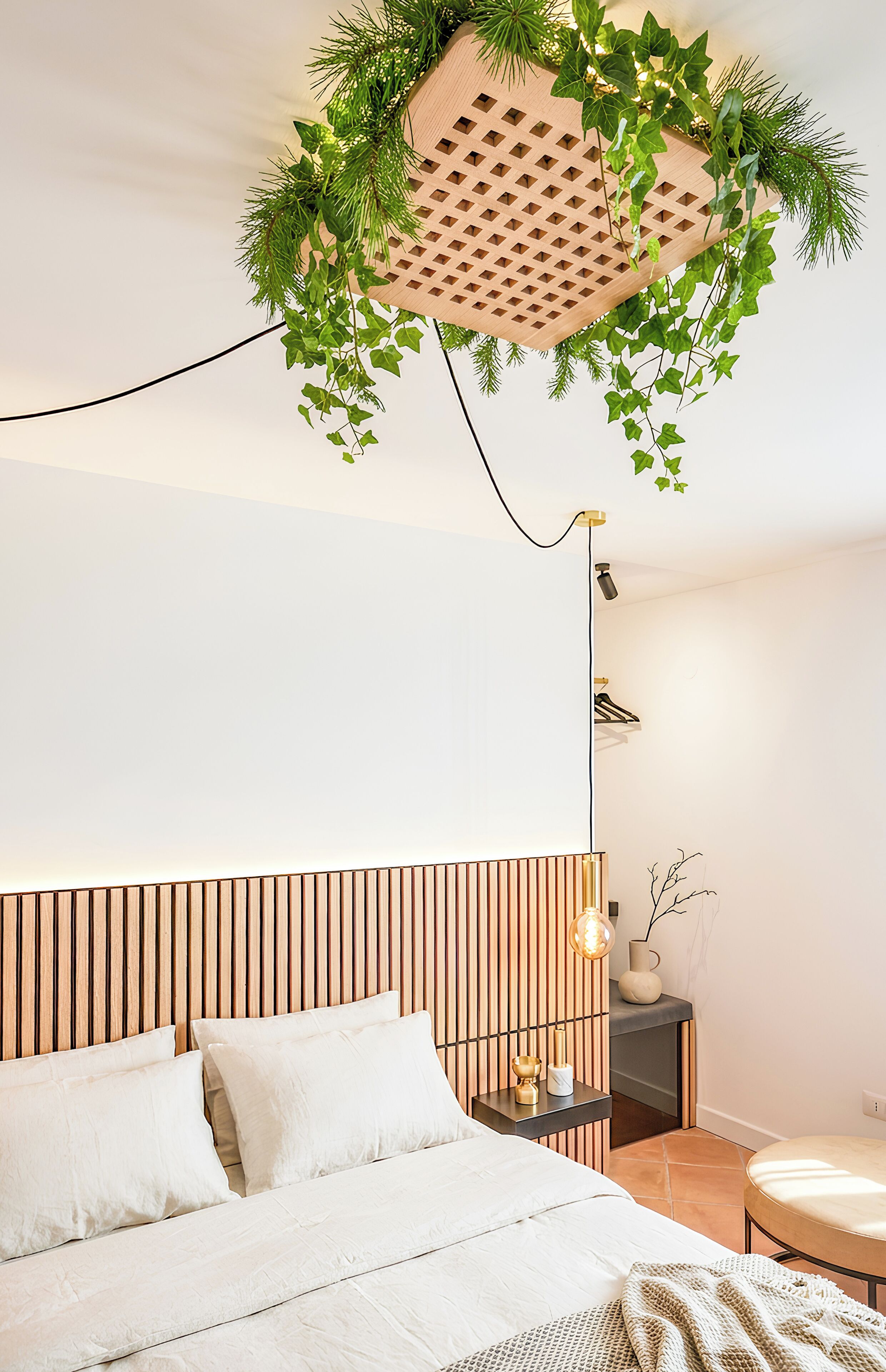 Une chambre à coucher avec un lit, une table de chevet, une lampe et une plante suspendue.