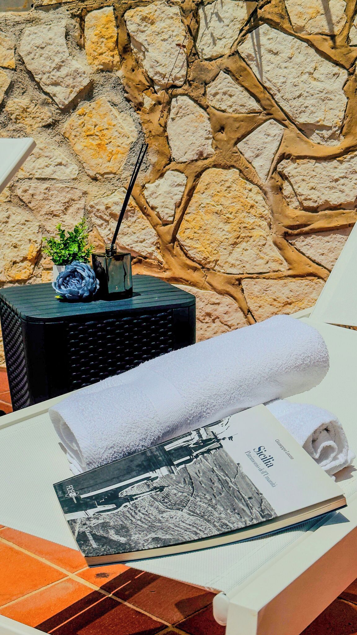 A room with a stone wall, a black speaker, a rolled white towel, and a magazine on a table.