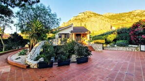 A house with a stone wall, a patio, and a mountain in the background. - Domus Dea - Appartamento Afrodite (Mondello)