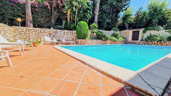 A swimming pool with a stone wall and tiled deck, surrounded by greenery and a stone wall. - Domus Dea - Appartamento Afrodite (Mondello)