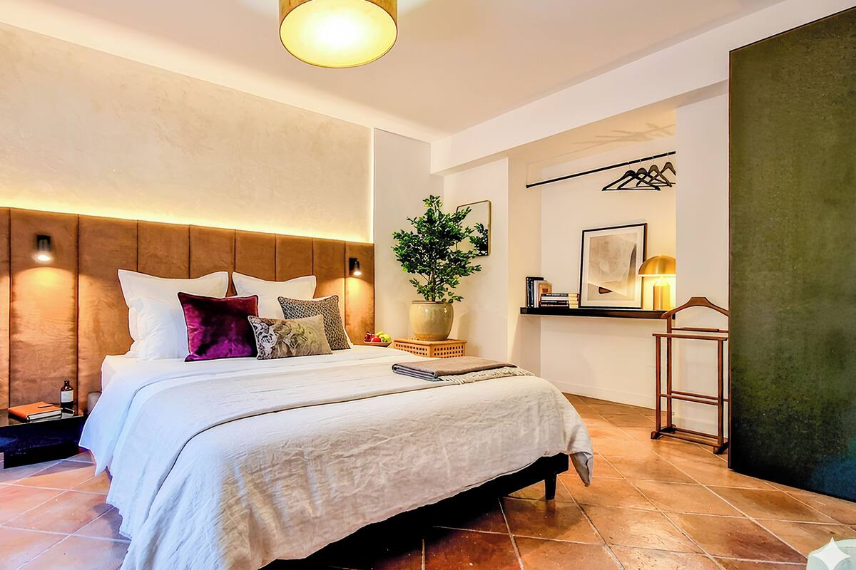 Un dormitorio moderno con una cama grande, una mesita de noche, una planta en maceta y un estante en la pared.