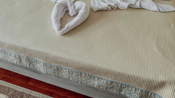 Een bed met een beige sprei en kussens, en witte handdoeken gerangschikt in de vorm van een hart.
