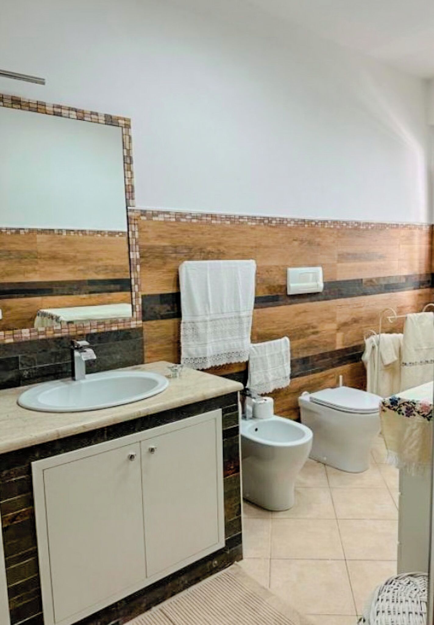 A bathroom with a sink, toilet, and bidet, featuring a tiled backsplash and a mirror.