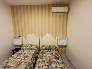 Ein kleines Hotelzimmer mit einem Bett, Streifenmuster-Tapete, einer Klimaanlage und Nachttischen mit Lampen.