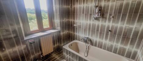 A modern bathroom with a freestanding bathtub, a toilet, and a window providing a view of greenery.