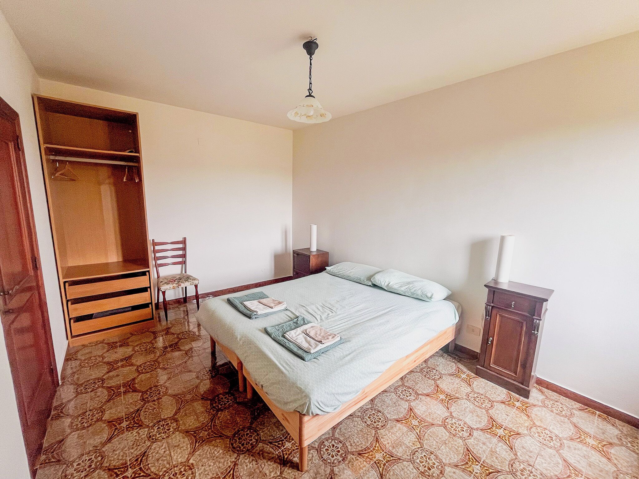 A bedroom with a bed, a chair, a wardrobe, and a nightstand.