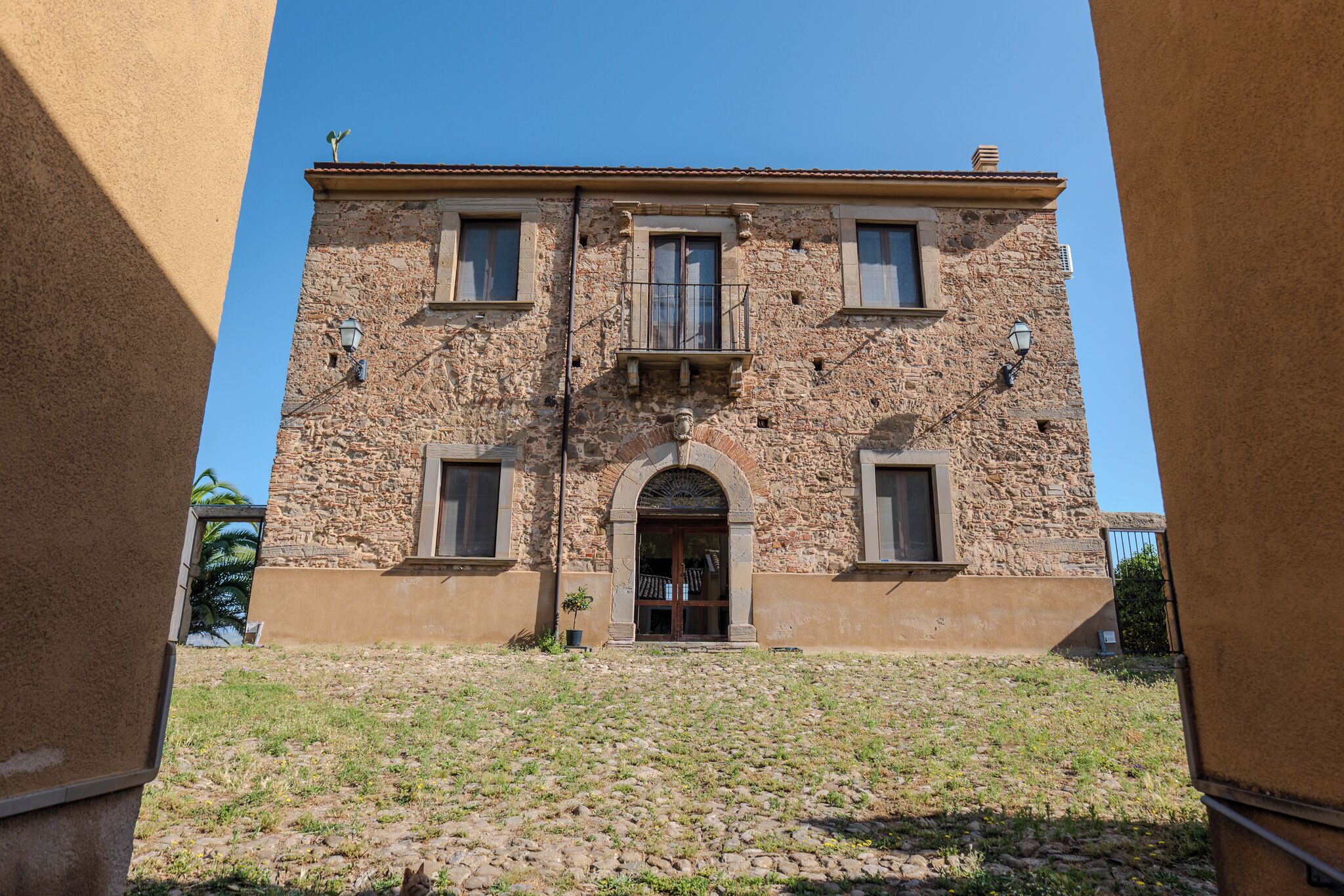 A stone building with a central entrance, two windows on each side, and a small balcony.