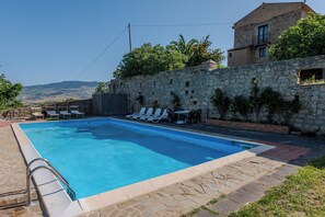 Una piscina con sillas de descanso, un muro de piedra y un edificio con balcón.