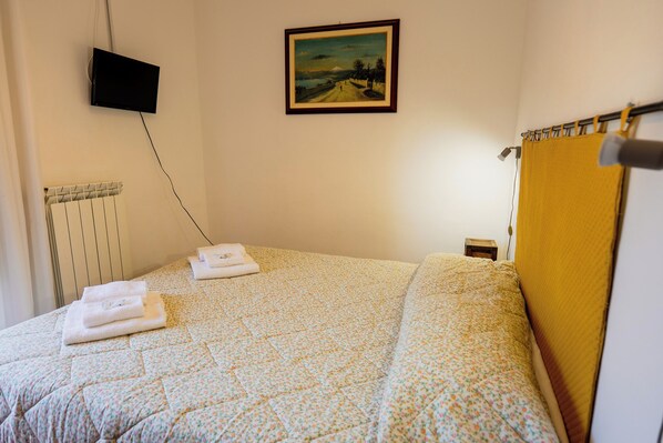 Un lit bien fait, recouvert d’une couvre-lit à motifs floraux, un tableau accroché au mur et un téléviseur fixé au-dessus.