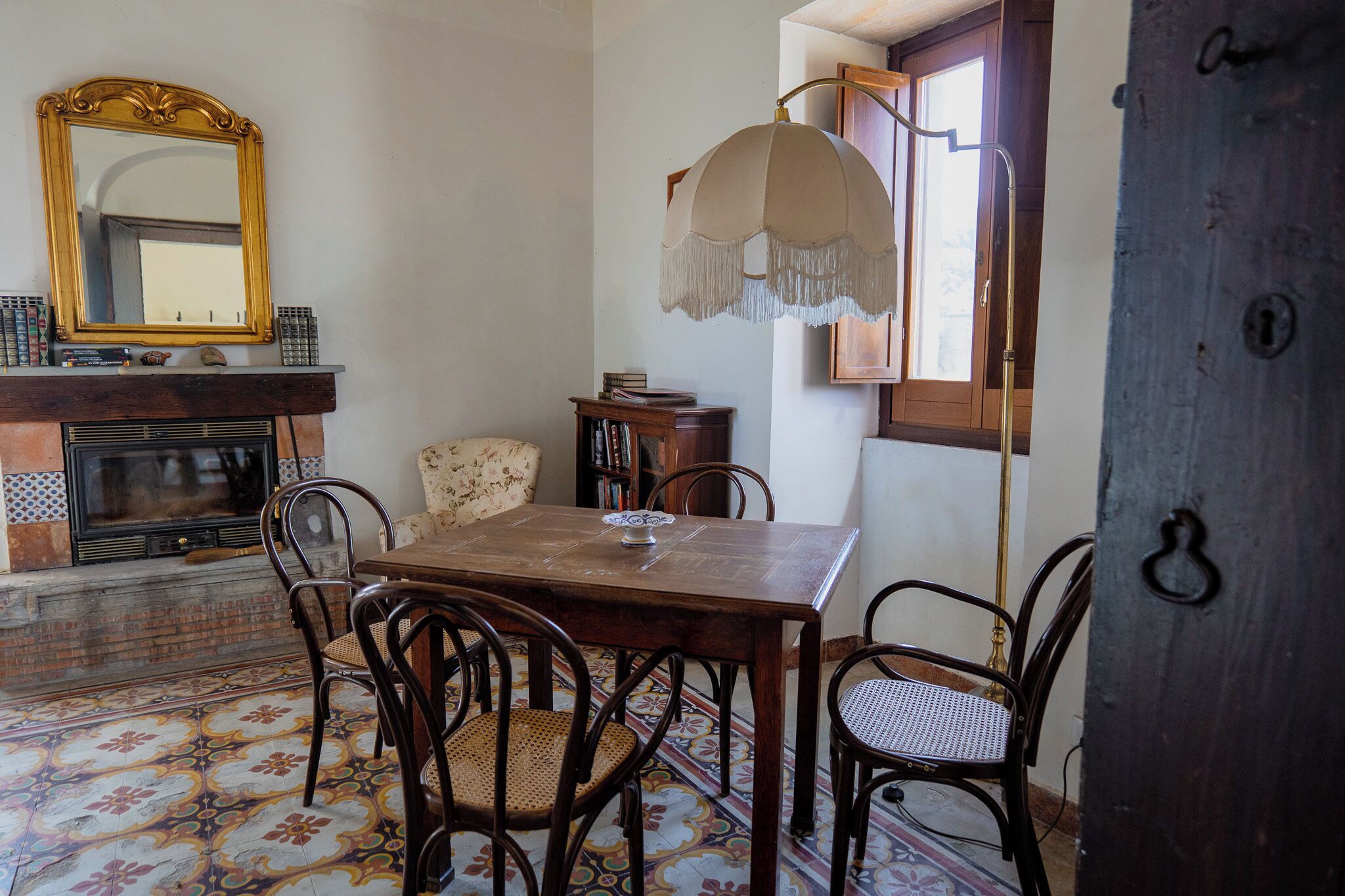 A dining area with a wooden table, chairs, a fireplace, a mirror, and a hanging lamp.