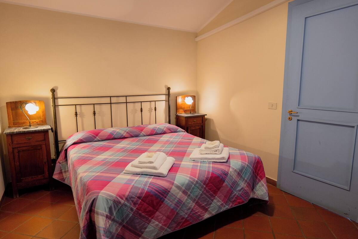 A bedroom with a bed, two bedside tables, a nightstand, a blue door, and a wall-mounted light fixture.