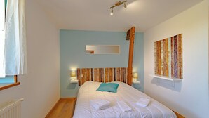 A bedroom with a bed, a wooden headboard, a mirror, wall art, and bedside lamps.