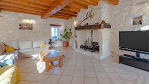 A cozy living room with a sofa, a wooden bench, a TV, a fireplace, and stone walls.