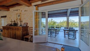 A room with a wooden ceiling, a dining area with tables and chairs, and a view of trees through a glass door.