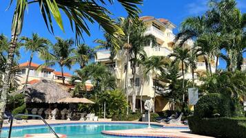 A swimming pool with a tiled edge, surrounded by palm trees and a building with a red roof in the background.