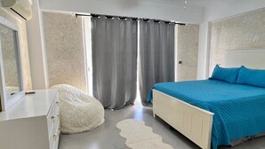 Quarto com cama, penteadeira, ventoinha no teto e janela com cortinas.