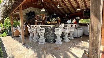 An outdoor bar area with a thatched roof, white wicker furniture, and a stone counter.