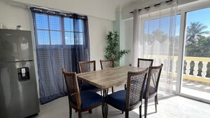 Uma sala de jantar com mesa e cadeiras, um refrigerador e um vaso de planta.