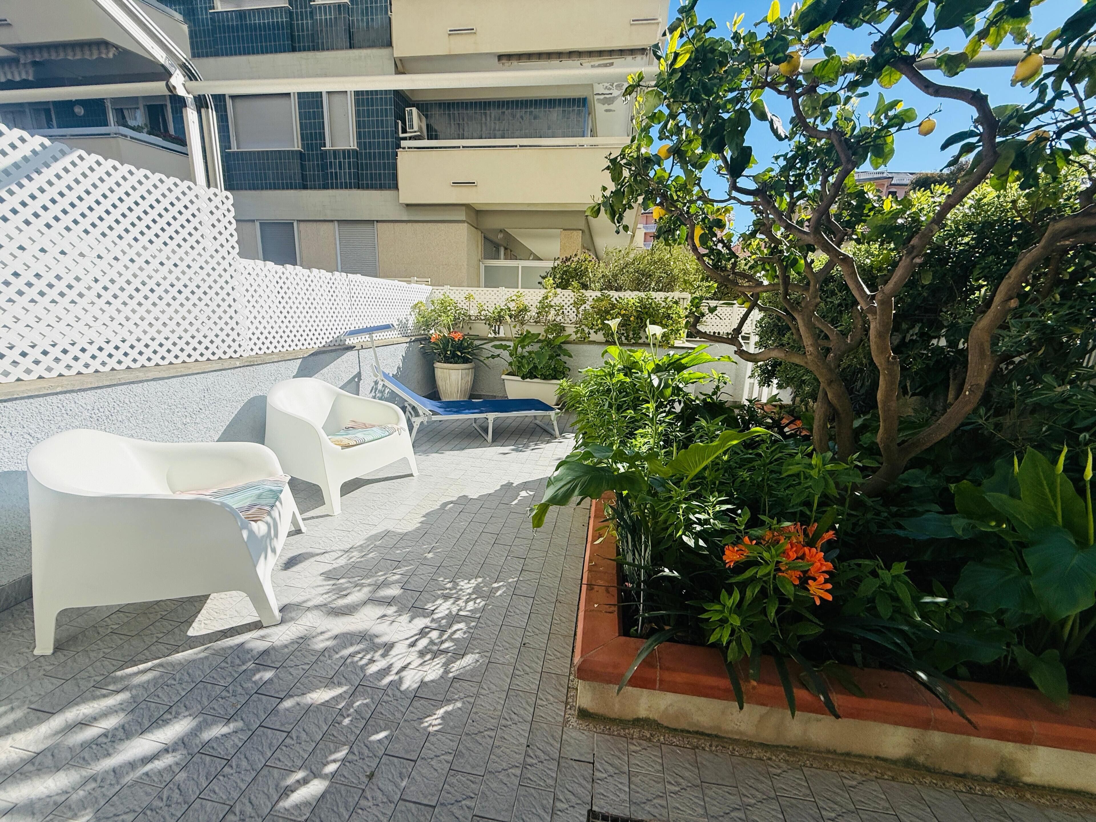 Eine Dachterrasse mit weißem Stuhl, blauem Liegestuhl und Topfpflanzen.
