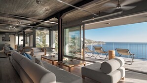 Ein modernes Interieur mit einer großen Couch, einem Couchtisch und einem Balkon mit Sitzgelegenheiten mit Blick auf das Meer.
