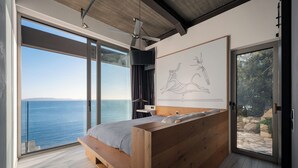 Ein modernes Schlafzimmer mit einem großen Bett, einem Deckenventilator, Meerblick und einem gerahmten Kunstwerk an der Wand.