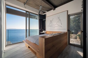 Ein modernes Schlafzimmer mit einem großen Bett, einem Deckenventilator, Meerblick und einem gerahmten Kunstwerk an der Wand.