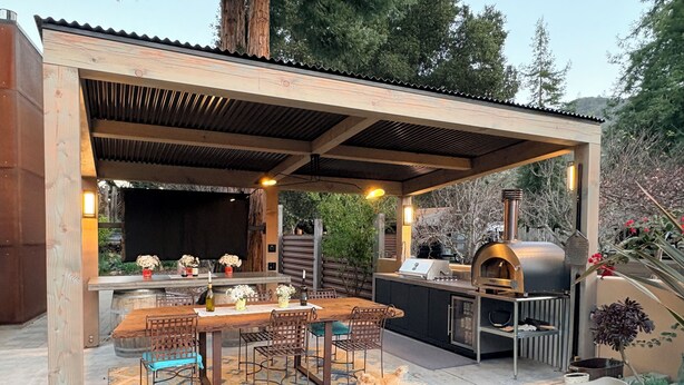 Un patio al aire libre con una mesa y sillas de madera, una parrilla y un horno para pizza.